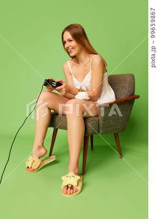 Studio shot of emotional young woman 25s years old wearing homewear, pajamas playing video game with joystick. Emotions, gaming concept. 99659867