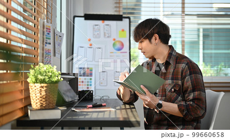 Side view of creative asian male working on mobile application software design project at modern modern home office Side view of creative asian male working on mobile application software design project at modern modern home office 99660658