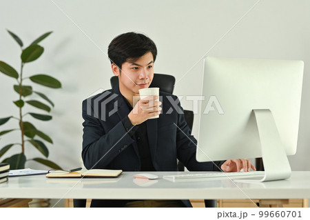 Successful asian man business entrepreneur drinking coffee and reading email on computer screen 99660701