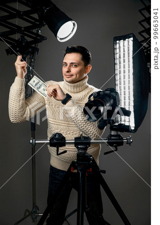 photographer with digital camera on tripod holding hundred dollar bills 99663041