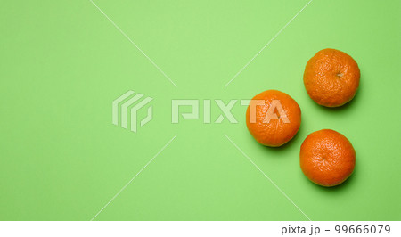 Three ripe mandarins on green background, top view. Ripe fruit 99666079