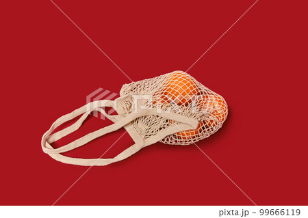 Oranges in a string bag on ruby red background 99666119