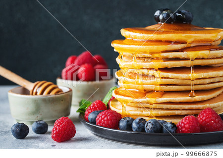 Delicious pancakes, with fresh blueberries, raspberry and maple syrup or honey on a dark background Delicious pancakes, with fresh blueberries, raspberry and maple syrup or honey on a dark background 99666875