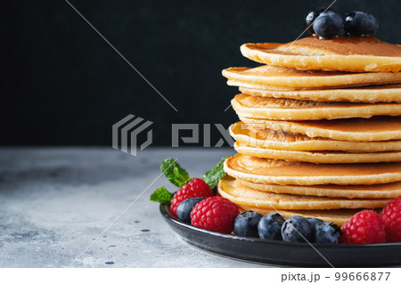 Delicious pancakes, with fresh blueberries, raspberry and maple syrup or honey on a dark background Delicious pancakes, with fresh blueberries, raspberry and maple syrup or honey on a dark background 99666877