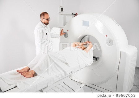 Medical computed tomography or MRI scanner. Male radiologist presses MRI button to examine female patient. Concept of healthcare and modern diagnostics. 99667055