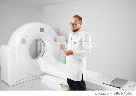 Portrait of doctor with medical computed tomography or MRI scanner. Radiologist holding and examining results of MRI. Concept of medicine, healthcare and modern diagnostics. 99667056