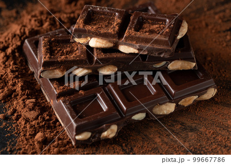 Dark and milk chocolate with nuts on a dark background sprinkled with cocoa powder. 99667786