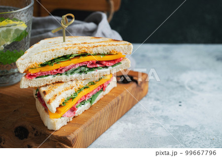 Two homemade sandwiches with sausage, cheese and arugula on a light concrete background Two homemade sandwiches with sausage, cheese and arugula on a light concrete background 99667796