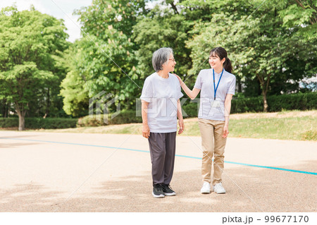 公園で運動・ウォーキング・歩く高齢者と介護士・看護師・理学療法士・運動指導員の女性 99677170