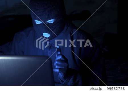 Masked hacker stealing data and personal identity information off laptop Masked hacker stealing data and personal identity information off laptop 99682728