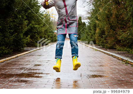 Jumping in puddle. Female legs in yellow rubber boots jumping on the puddle. Carefree young woman in rain boots jumps Jumping in puddle. Female legs in yellow rubber boots jumping on the puddle. Carefree young woman in rain boots jumps 99684979