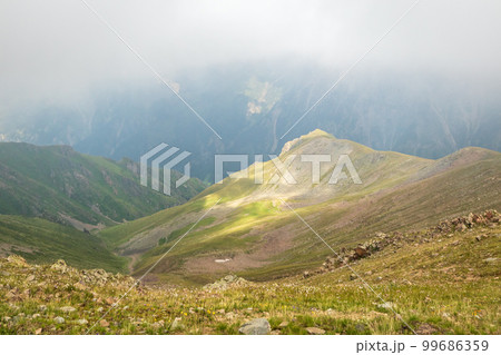 Mysterious minimalist high-altitude picturesque mountain landscape with clouds touching large peaks in Almaty mountains of Kazakhstan nature 99686359