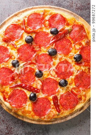 Diavola pizza with sausage, cheese, tomato sauce, chili peppers and black olives close-up on a wooden board. Vertical top view Diavola pizza with sausage, cheese, tomato sauce, chili peppers and black olives close-up on a wooden board. Vertical top view 99687272