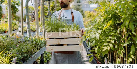 Midsection of male gardener walking and holding box. Garden centre shop 99687303