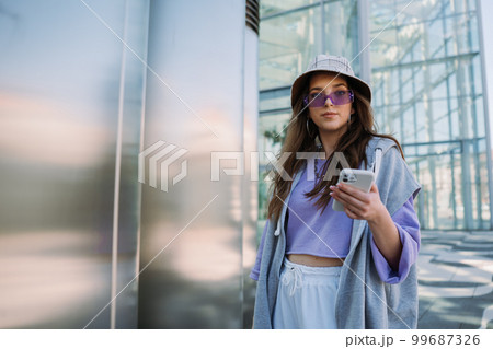 Cool young girl looking to camera and holding mobile phone.  99687326