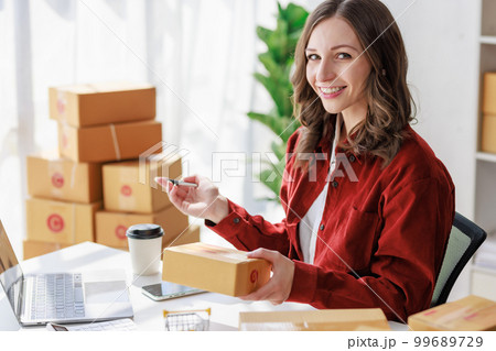 Concept of parcel delivery and selling online,Female seller or retailer write the customer's address on the parcel box to prepare for delivery and using laptop checking day's sales on the online store Concept of parcel delivery and selling online,Female seller or retailer write the customer's address on the parcel box to prepare for delivery and using laptop checking day's sales on the online store 99689729
