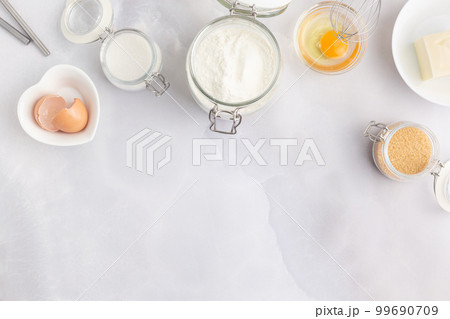 Various baking ingredients - flour, eggs, sugar, butter and kitchen utensils on grey background. Top 99690709