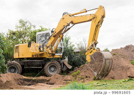 A bucket of excavator with a pile of sand and a ground background. Industrial work on the construction site A bucket of excavator with a pile of sand and a ground background. Industrial work on the construction site 99691605