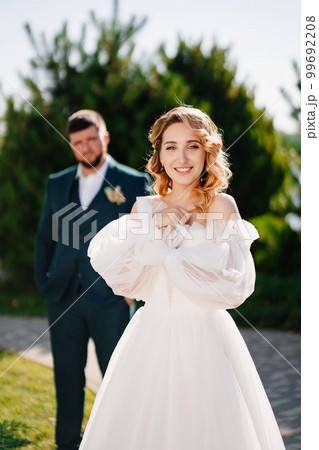a bride in a delicate dress stands in front of the groom in the park. 99692208