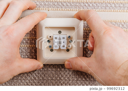 male hand replaces or repairs the light switch on the wall with brown wallpaper. 99692312