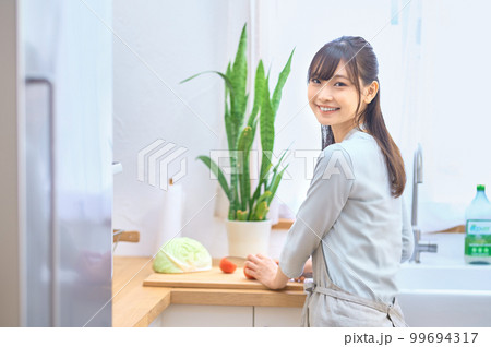 キッチンで料理するエプロン姿の若い主婦 99694317