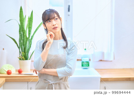 キッチンで考え事をするエプロン姿の若い主婦 キッチンで考え事をするエプロン姿の若い主婦 99694444