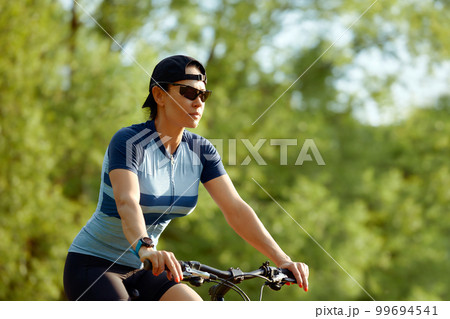 Happy brunette girl in sportswear riding a bike in the park. Happy brunette girl in sportswear riding a bike in the park. 99694541