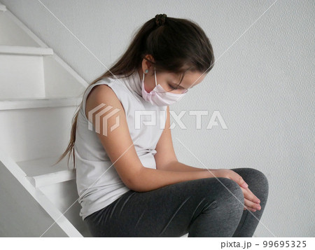 Student girl wearing a mask seating on stairs after COVID-19 quarantine and lockdown, sad and tired of not going to school with her friends. 99695325