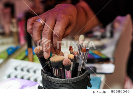 A hand chooses between several makeup brushes inside a beaker A hand chooses between several makeup brushes inside a beaker 99696046