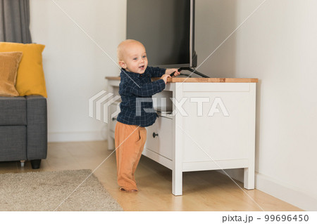 Toddler baby boy open cabinet drawer with his hand. Child explore what is in cabinet. Baby curiosity and child development stages Toddler baby boy open cabinet drawer with his hand. Child explore what is in cabinet. Baby curiosity and child development stages 99696450