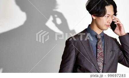 真剣な表情で通話をするスーツ姿の若い男性 99697283