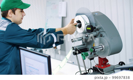 The worker changes paper roll with marking stickers on a machine with automated marking. 99697838