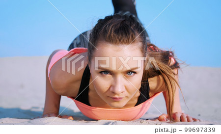 Healthy, young beautiful woman doing, performs push-ups,on the beach, at sunrise, Makes exercises for balance and coordination, deep muscle tone. Close-up, portrait 99697839