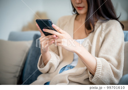 Happy young asian woman relax on comfortable couch at home texting messaging on smartphone Happy young asian woman relax on comfortable couch at home texting messaging on smartphone 99701610