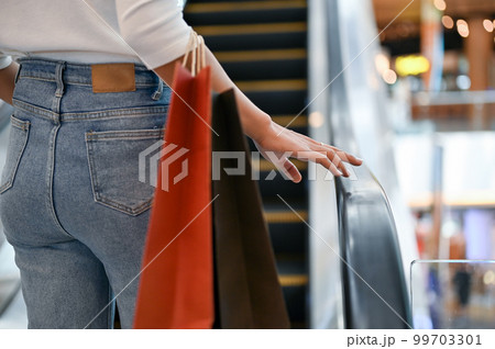 A woman with her shopping bags taking the escalator up to the next floor at the mall. A woman with her shopping bags taking the escalator up to the next floor at the mall. 99703301