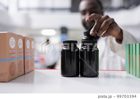 African american pharmacist taking medication from drugstore shelf closeup, selective focus on bottles. Pharmacy medic putting pills close up, vitamins selling, chemist front view African american pharmacist taking medication from drugstore shelf closeup, selective focus on bottles. Pharmacy medic putting pills close up, vitamins selling, chemist front view 99703394