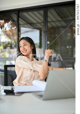 Relaxed millennial Asian businesswoman stretching her arms, taking a break from work Relaxed millennial Asian businesswoman stretching her arms, taking a break from work 99703787