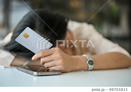 Tired and sad Asian woman laid her head down on the table, holding a credit card 99703815