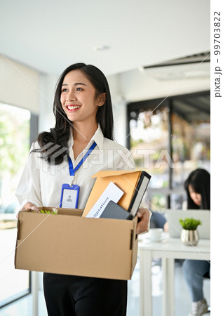Beautiful Asian female office worker holding a cardboard box with her belongings, happy to resign. 99703822