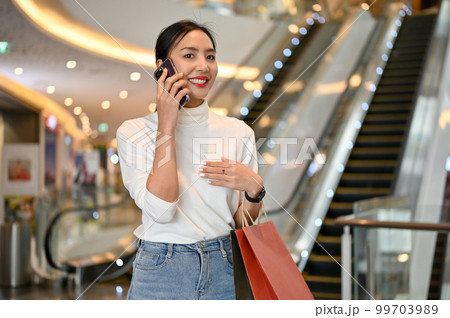 Gorgeous Asian woman is on the phone while shopping alone at the luxury shopping center. Gorgeous Asian woman is on the phone while shopping alone at the luxury shopping center. 99703989