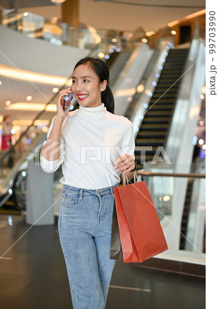 Attractive Asian woman is on the phone with her friend while shopping at the mall. Attractive Asian woman is on the phone with her friend while shopping at the mall. 99703990