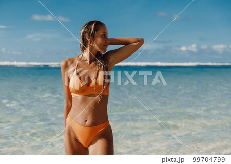 Portrait of tanned woman in yellow bikini at ocean beach. 99704799
