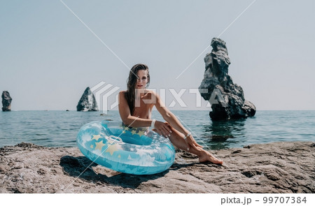 Woman summer sea. Happy woman swimming with inflatable donut on the beach in summer sunny day, surrounded by volcanic mountains. Summer vacation concept. 99707384