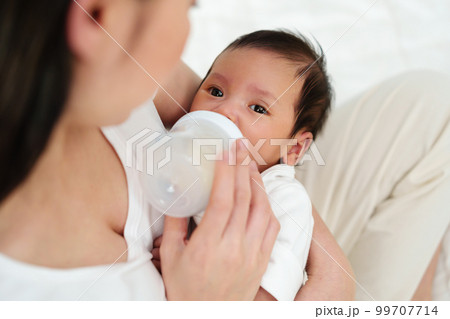 mother feeding milk bottle to her newborn baby on bed mother feeding milk bottle to her newborn baby on bed 99707714