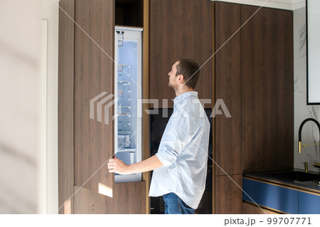 A man stands near an open empty refrigerator and studies the contents A man stands near an open empty refrigerator and studies the contents 99707771