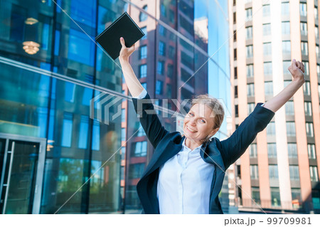 Happy business woman showing thumbs up while standing outdoors against office 99709981