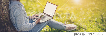 Woman with laptop sitting on the grass in the natural park. 99713657