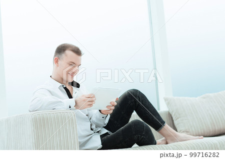 smiling man with digital tablet sitting on sofa in his living room 99716282