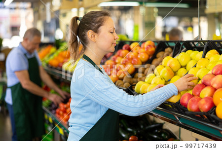 Middle-aged saleswoman putting apples on food stall in grocery store 99717439