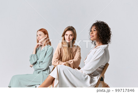 Group portrait of different beautiful young women in elegant dresses sitting on chairs over light background. Concept of beauty, fashion, business, ad Group portrait of different beautiful young women in elegant dresses sitting on chairs over light background. Concept of beauty, fashion, business, ad 99717846